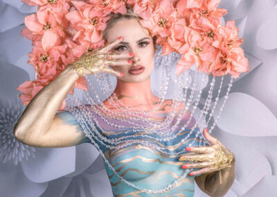 A stunning fine art portrait by Victoria Machin Photography, featuring a model adorned with a grand floral headpiece, intricate body paint, and gold metallic accents. This luxury high-fashion image blends glamour, beauty, and avant-garde art, establishing itself as a world-class fine art composition.