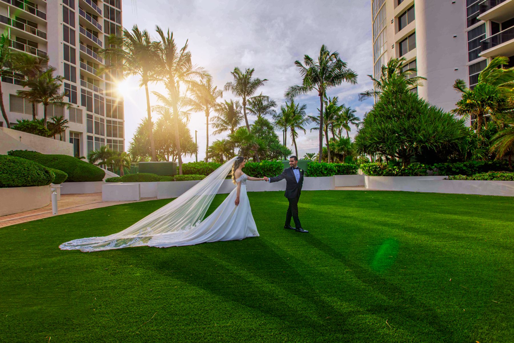 Elegant Wedding Portrait at Trump Towers Sunny Isles | Victoria Machin Photography Bride and groom holding hands on a lush green lawn with sunset light and tropical palm trees at Trump Towers Sunny Isles, photographed by Victoria Machin.