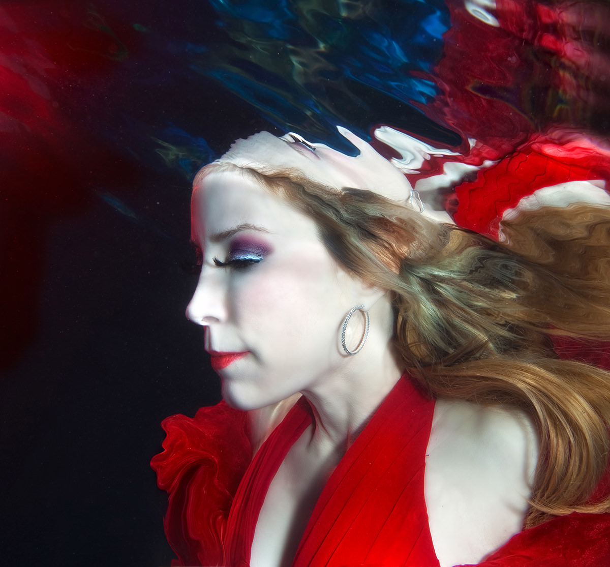 Lynn Martinez floats gracefully underwater in a red gown during an artistic underwater photo session by Victoria Machin Photography.