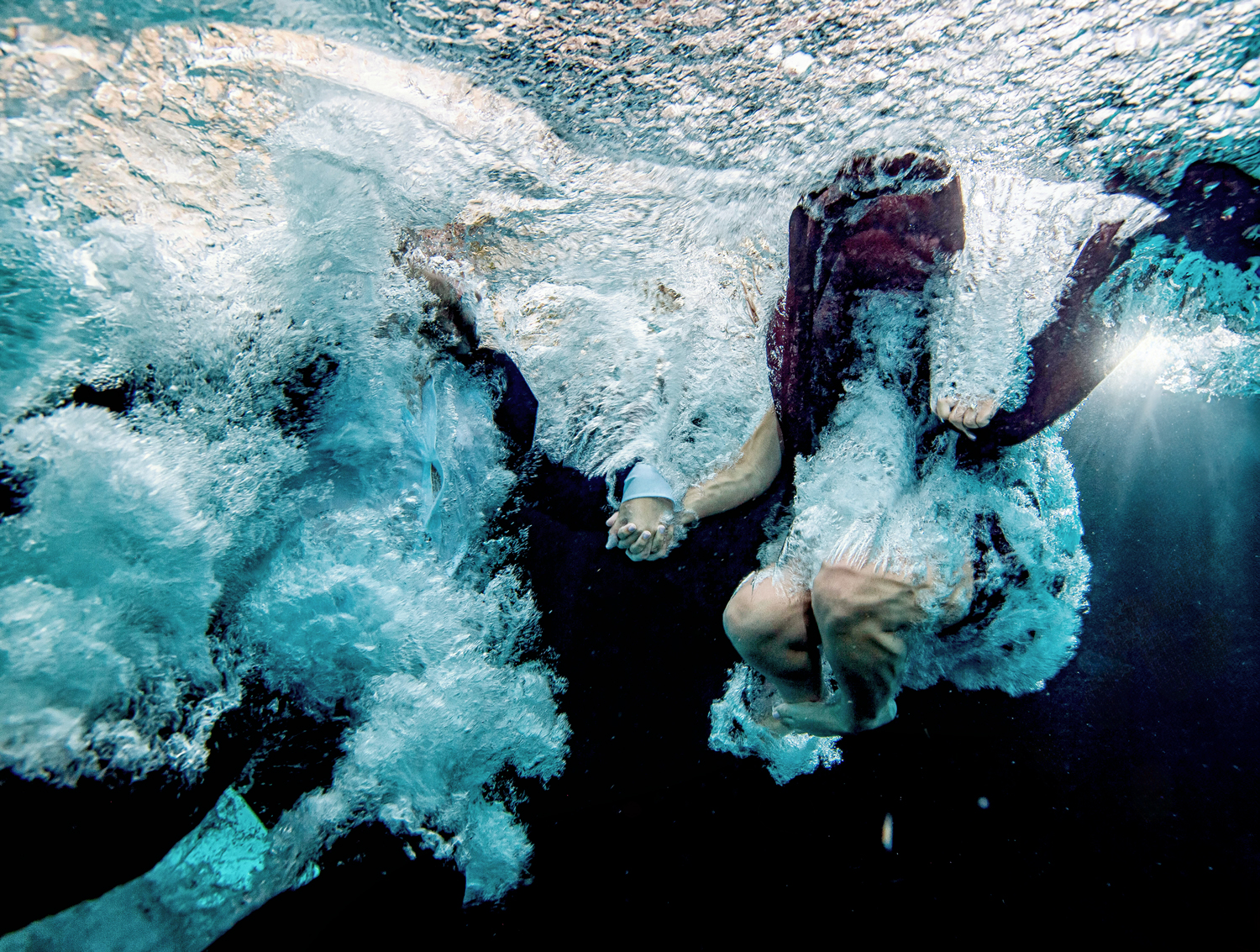 Couple holding hands while diving into water, captured mid-splash in an artistic underwater engagement photoshoot in Miami by Victoria Machin Photography.