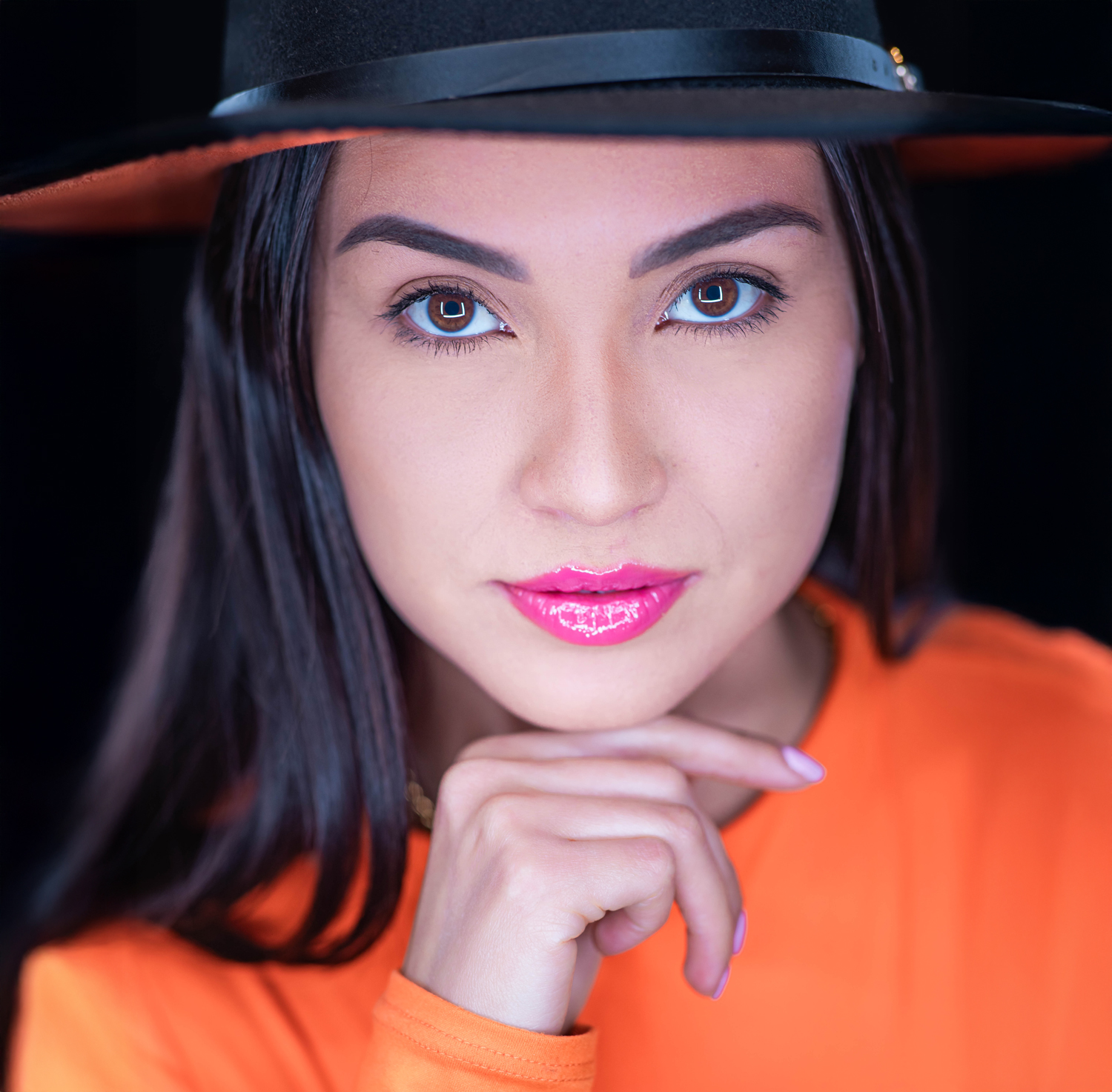 Confident woman in a black wide-brim hat and orange top posing for a professional headshot by Victoria Machin Photography in Miami.