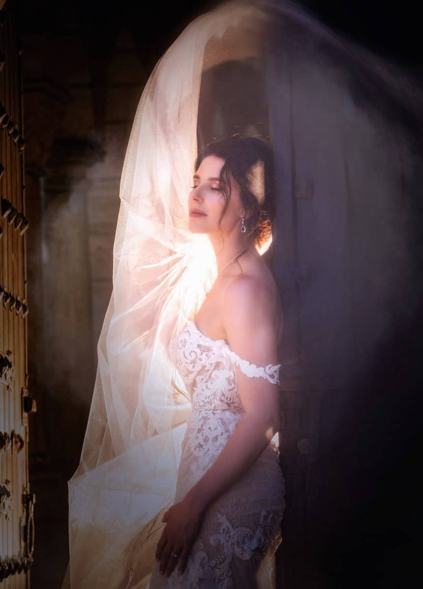 Bride in backlit veil beside a cathedral door