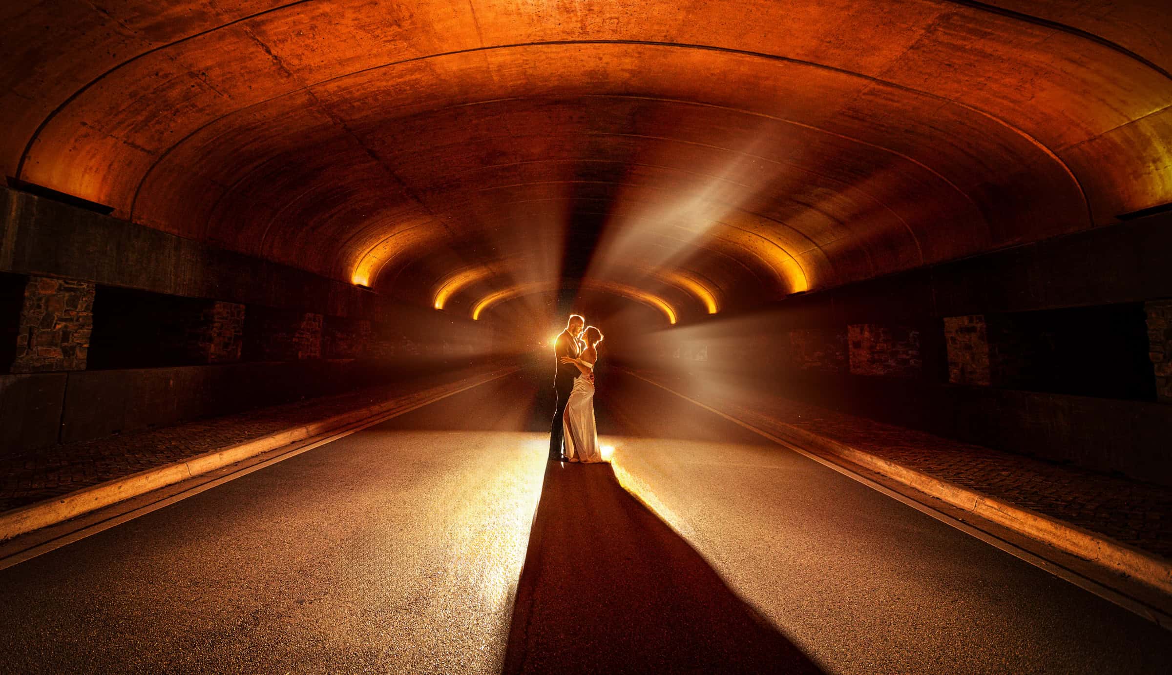 Bride and groom embracing in a beam of light inside a warmly lit tunnel