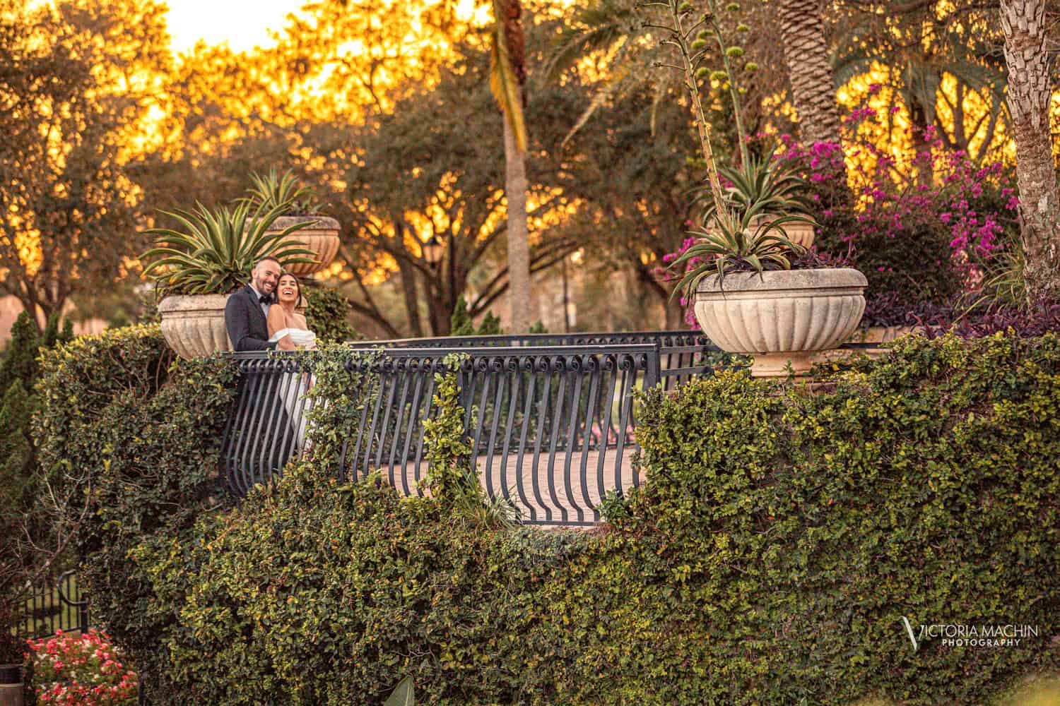Bride and groom laughing on a garden terrace at sunset, framed by bougainvillea and stone planters, Parkland Golf Club