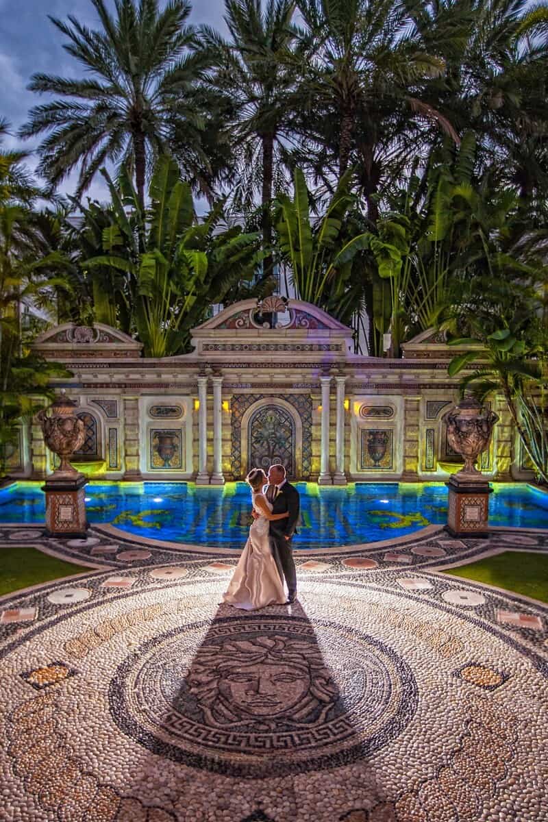 Bride and groom embracing on a mosaic courtyard beside an ornate pool at dusk