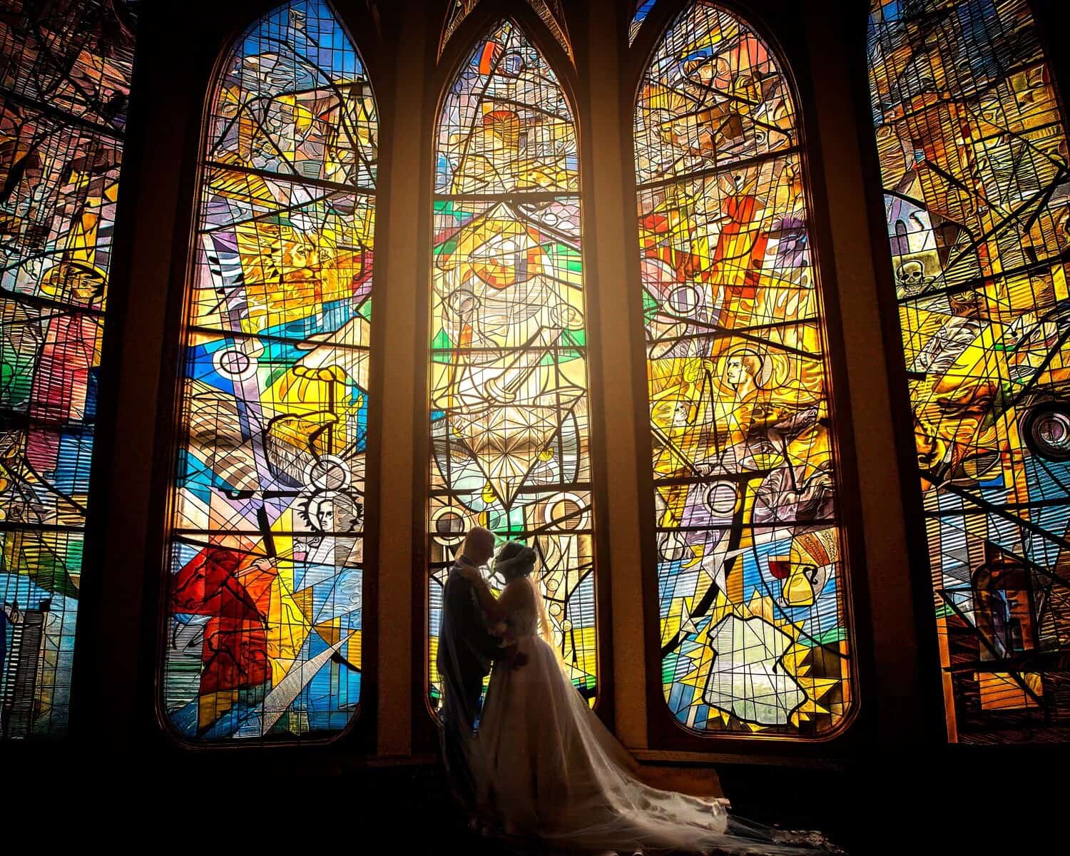 Bride and groom embracing before towering stained-glass cathedral windows