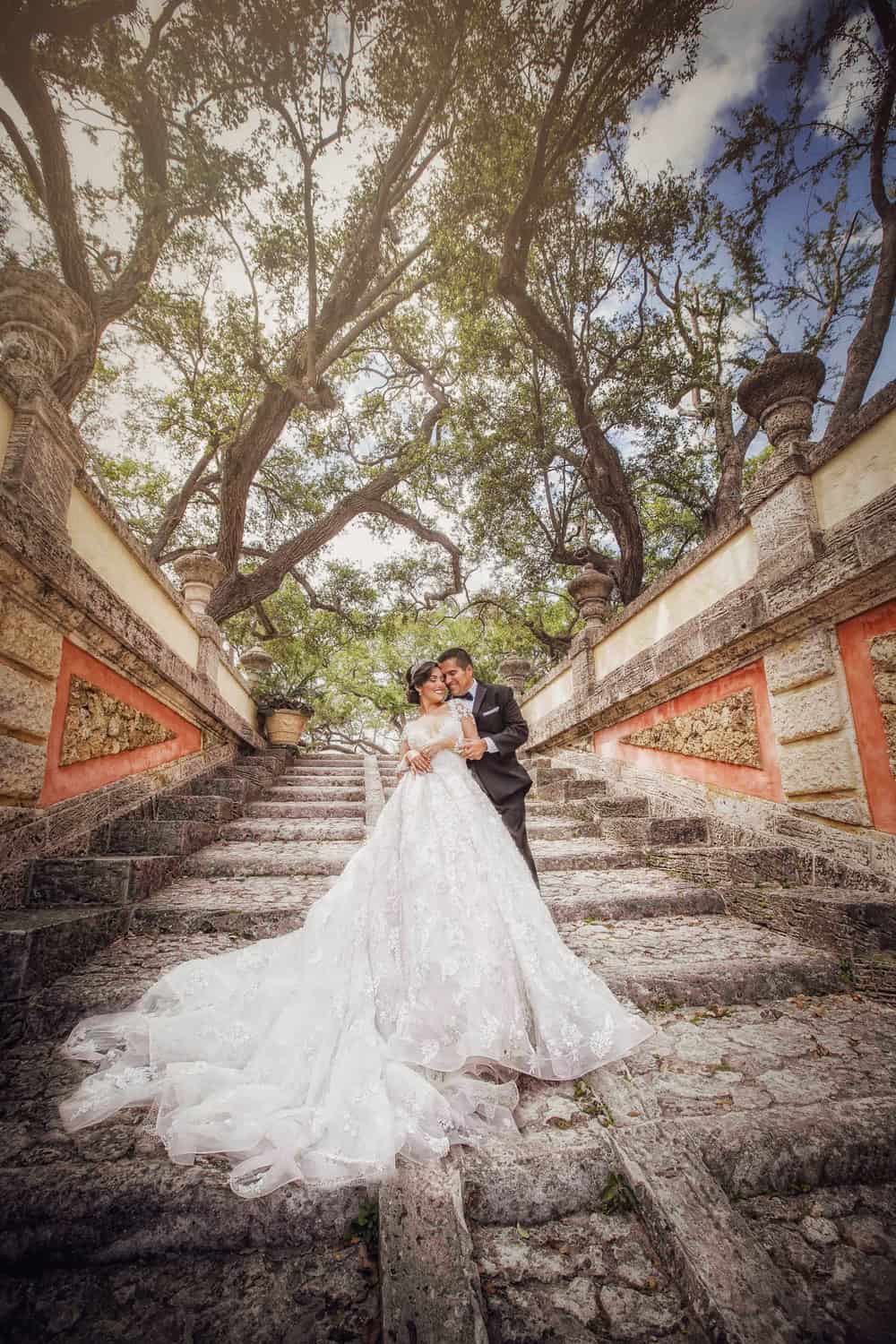 Bride and groom embracing on a coral stone staircase beneath sprawling oak trees