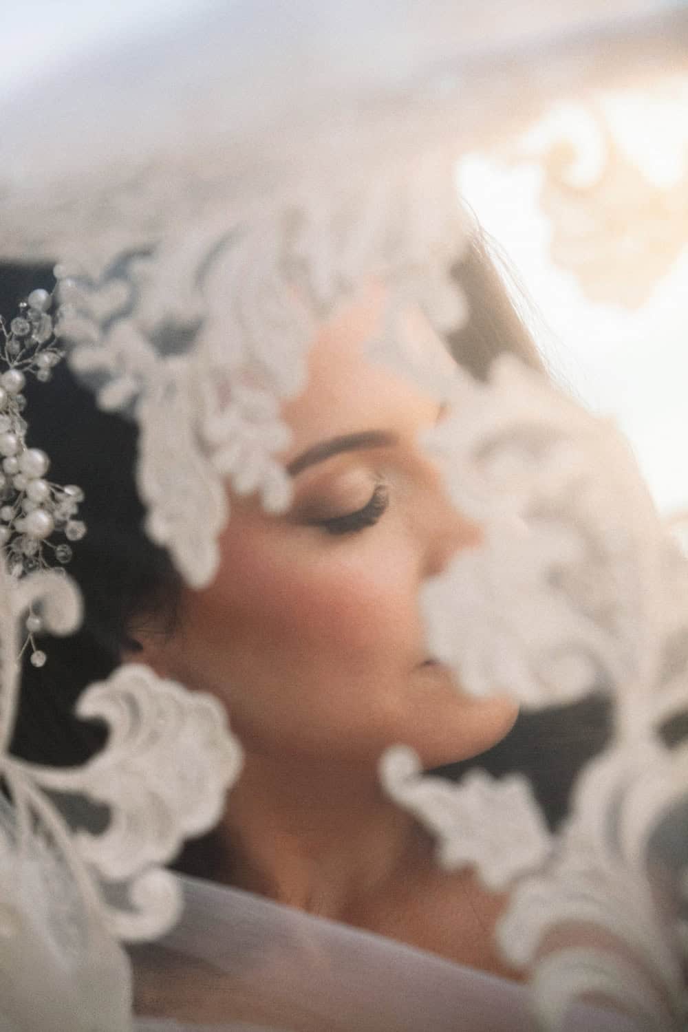 Close-up of a bride with eyes closed beneath a lace-edged veil at sunset