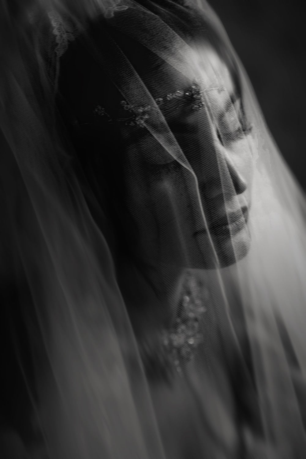 Bride’s face in soft focus beneath layers of tulle veil, black and white
