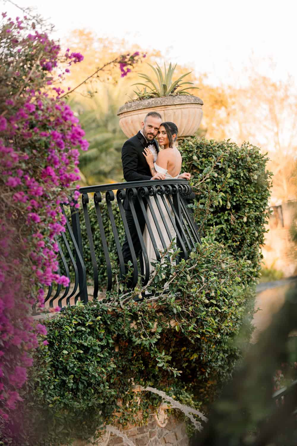 Bride and groom on a garden balcony framed by bougainvillea at golden hour