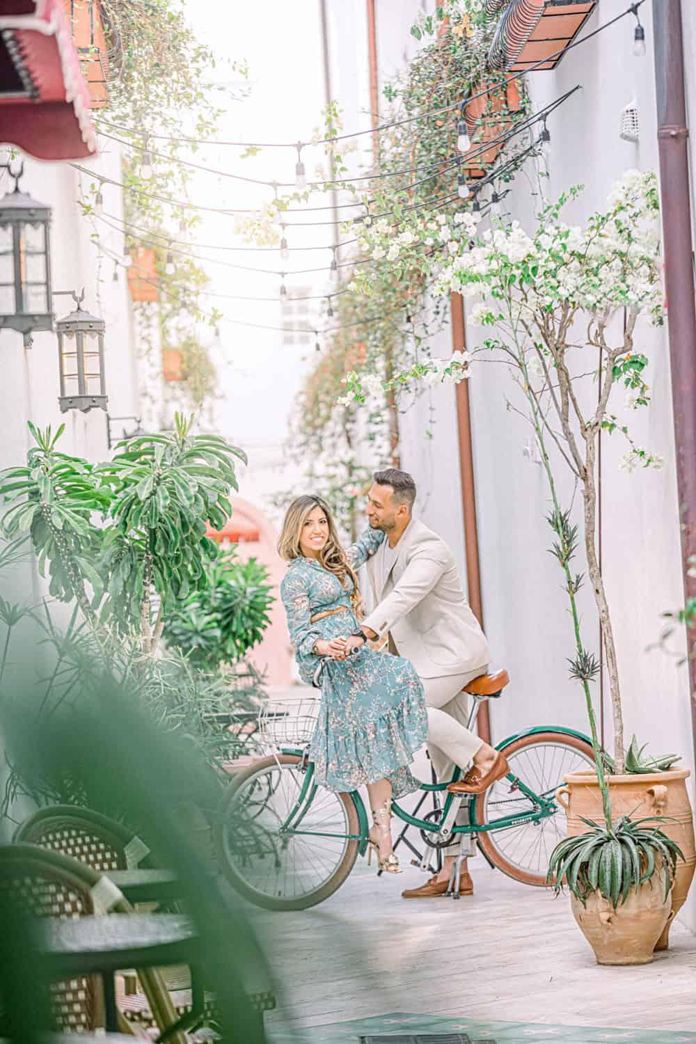 Couple on a green bicycle in a whitewashed alley of bougainvillea and string lights