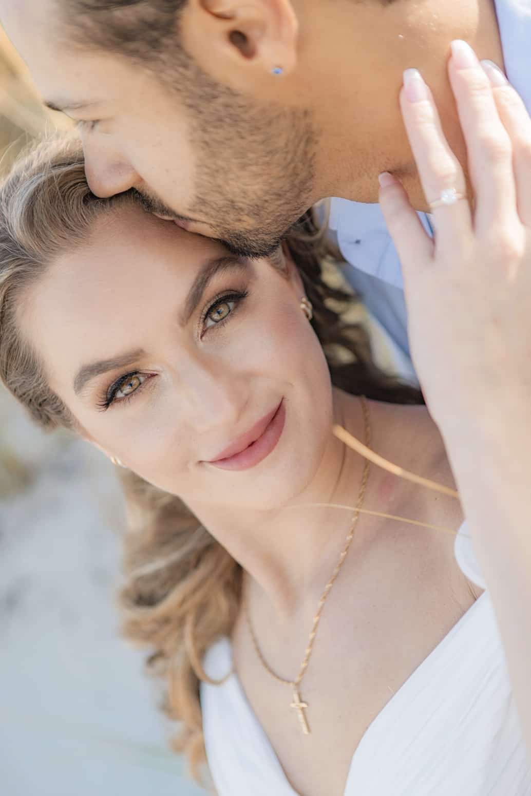 Close-up of a bride-to-be smiling as her fiancé kisses her forehead, ring in view