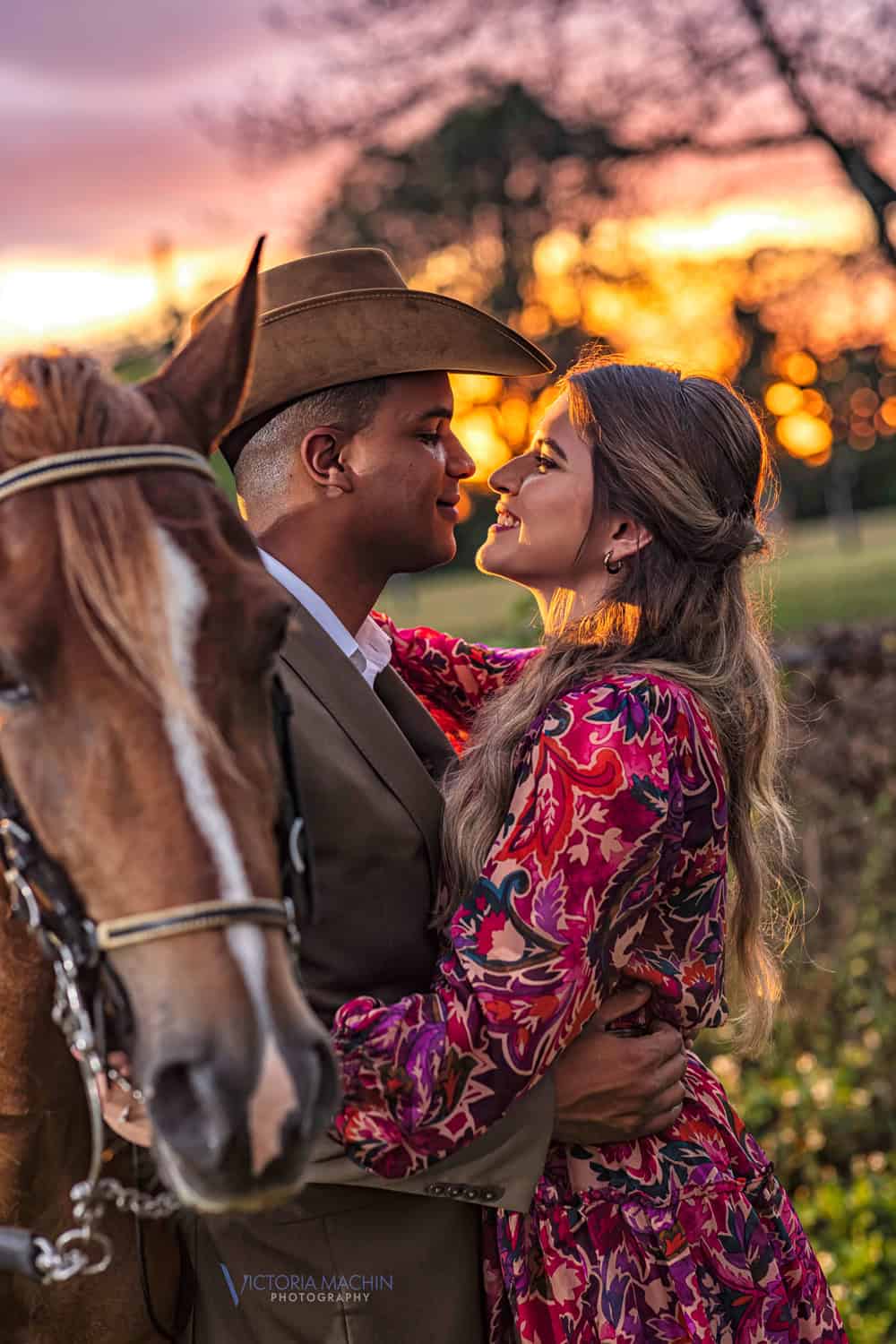 Couple about to kiss beside their horse at sunset, he in a cowboy hat