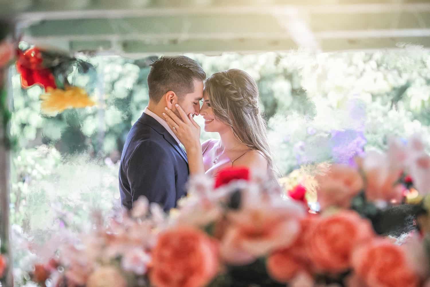 Couple touching foreheads behind a blur of roses in a garden
