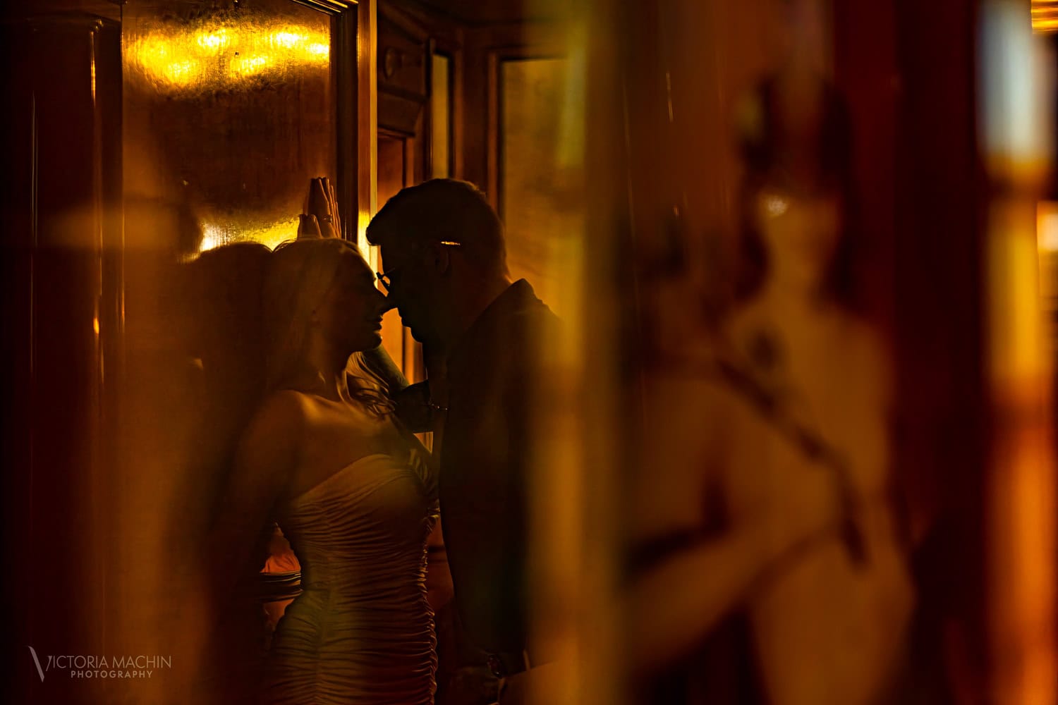 Silhouetted couple nose to nose in golden light reflected through glass
