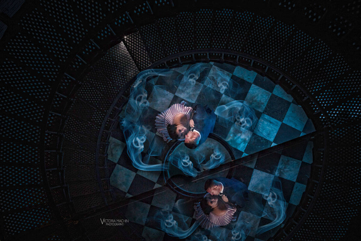 Couple seen from above at the base of a spiral staircase, wrapped in blue smoke