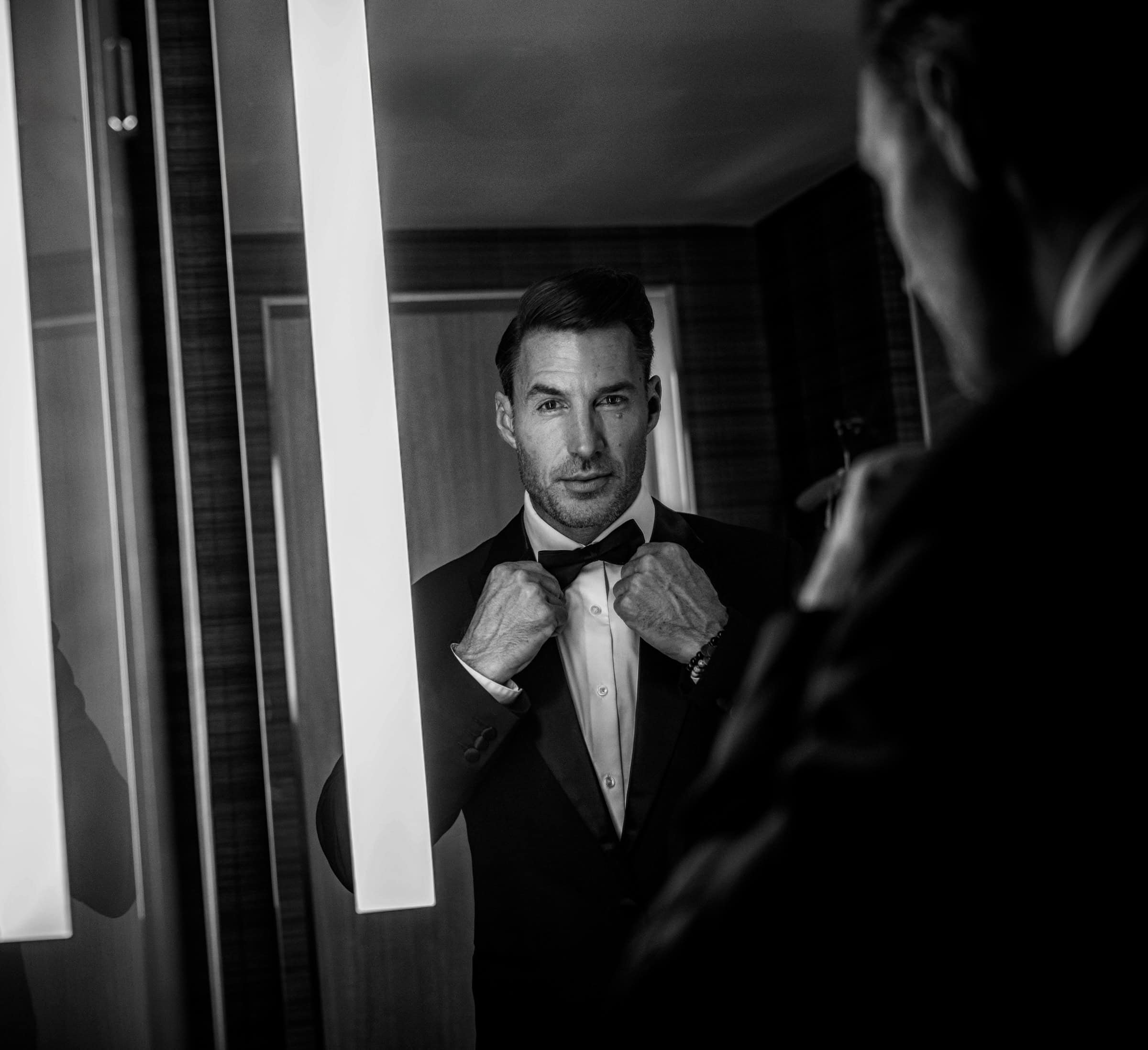Groom straightening his bow tie in the mirror, black and white