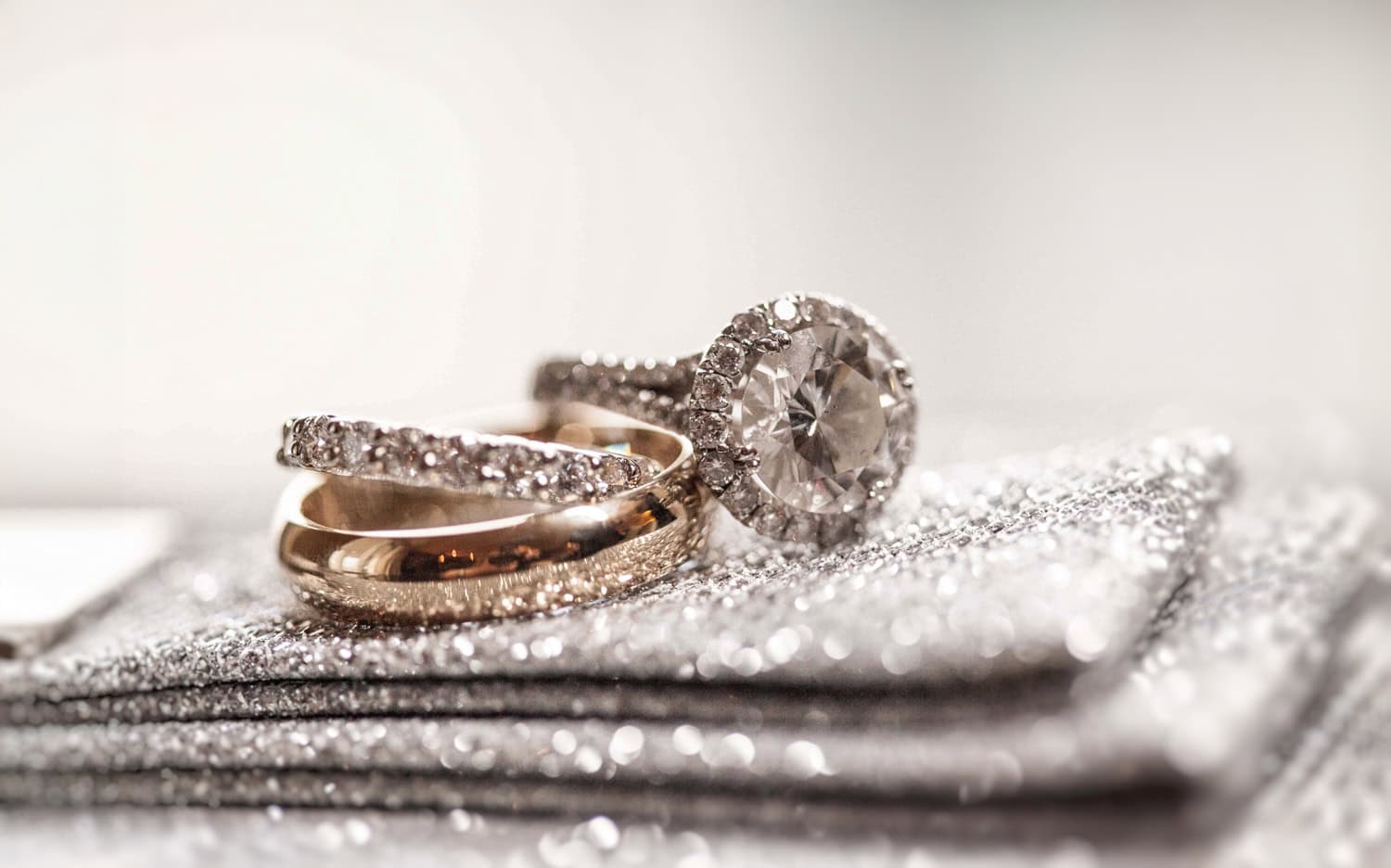 Halo engagement ring and gold wedding bands resting on a sparkling clutch