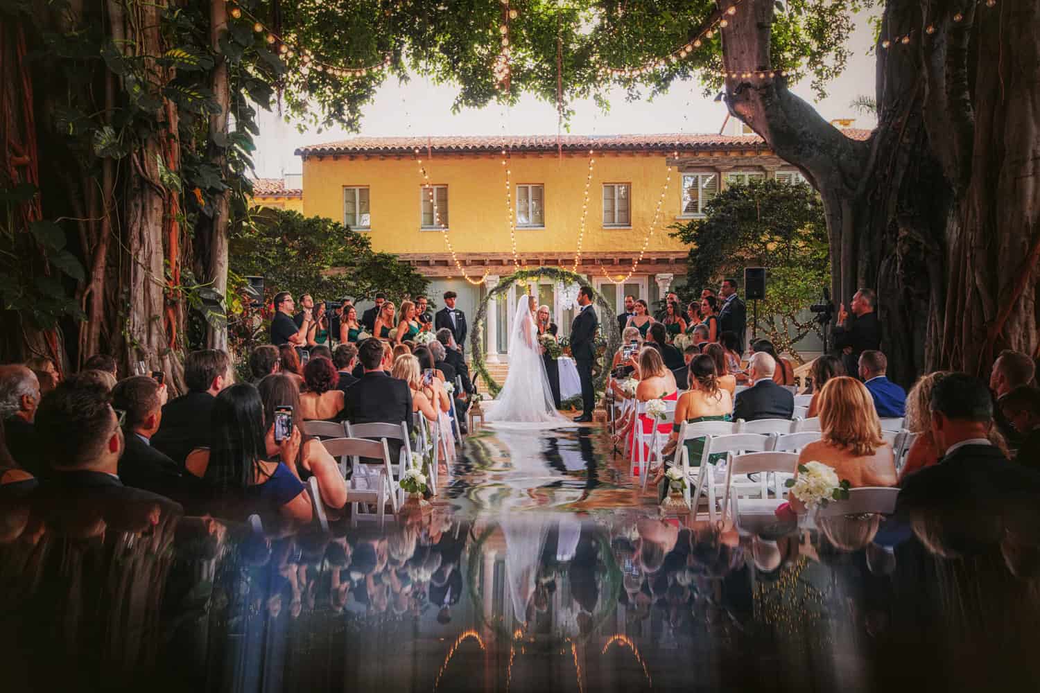 Outdoor wedding ceremony beneath banyan trees with string lights