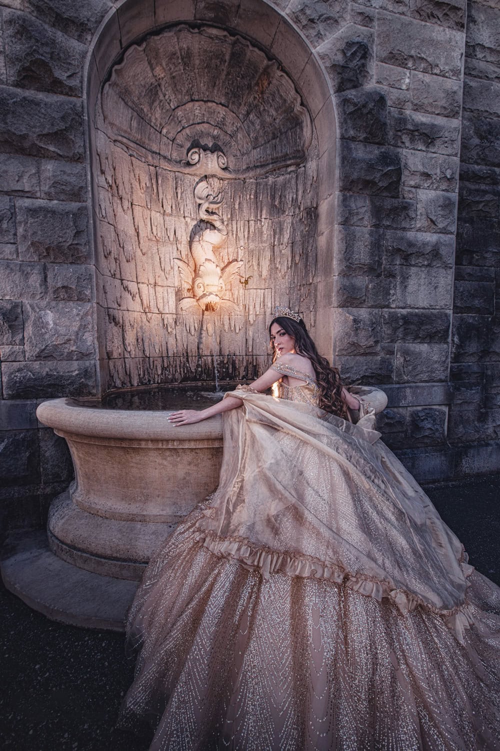 Quinceañera in a champagne beaded gown leaning on a stone fountain at The Biltmore Estate