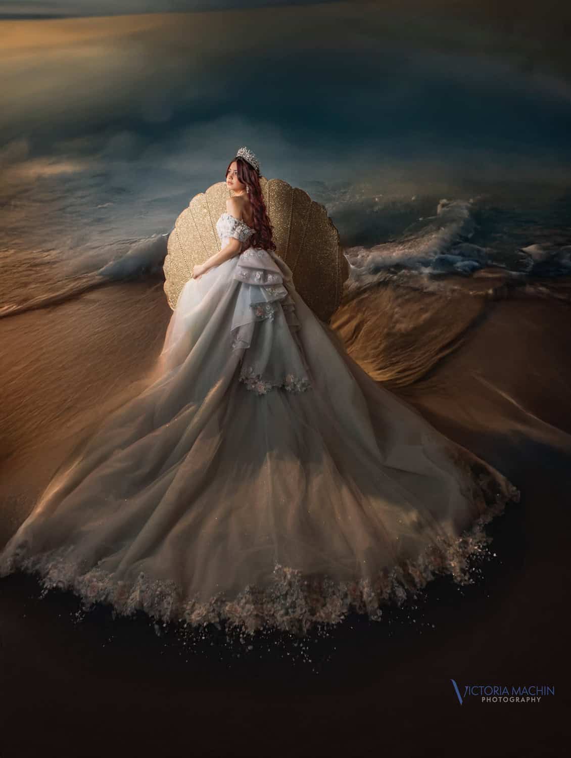Fine-art quinceañera portrait in a flowing gown seated in a golden seashell at the ocean’s edge