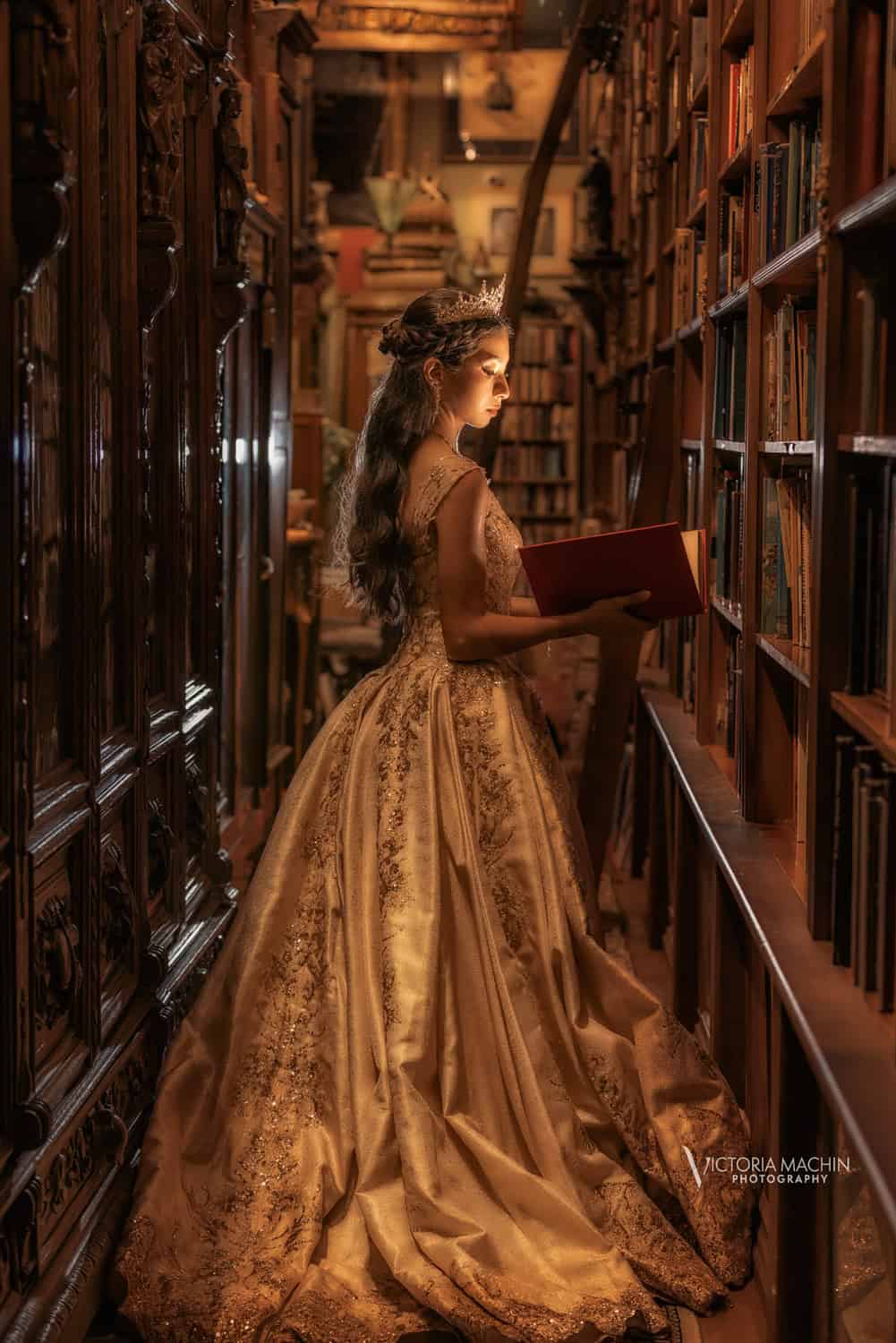 Quinceañera in a gold gown reading in a warmly lit antique bookstore