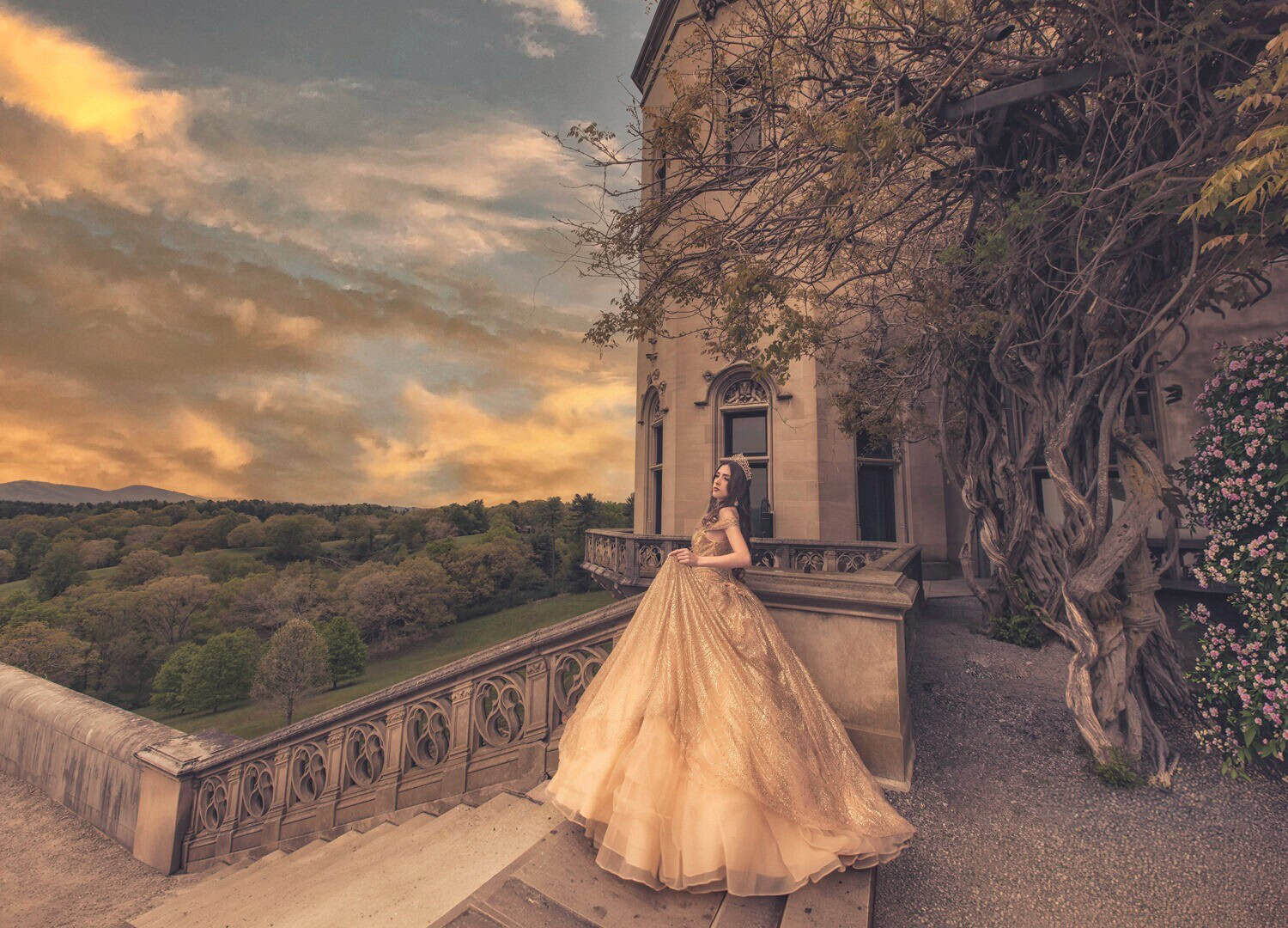 Quinceañera in a gold gown on a castle terrace overlooking rolling hills at sunset