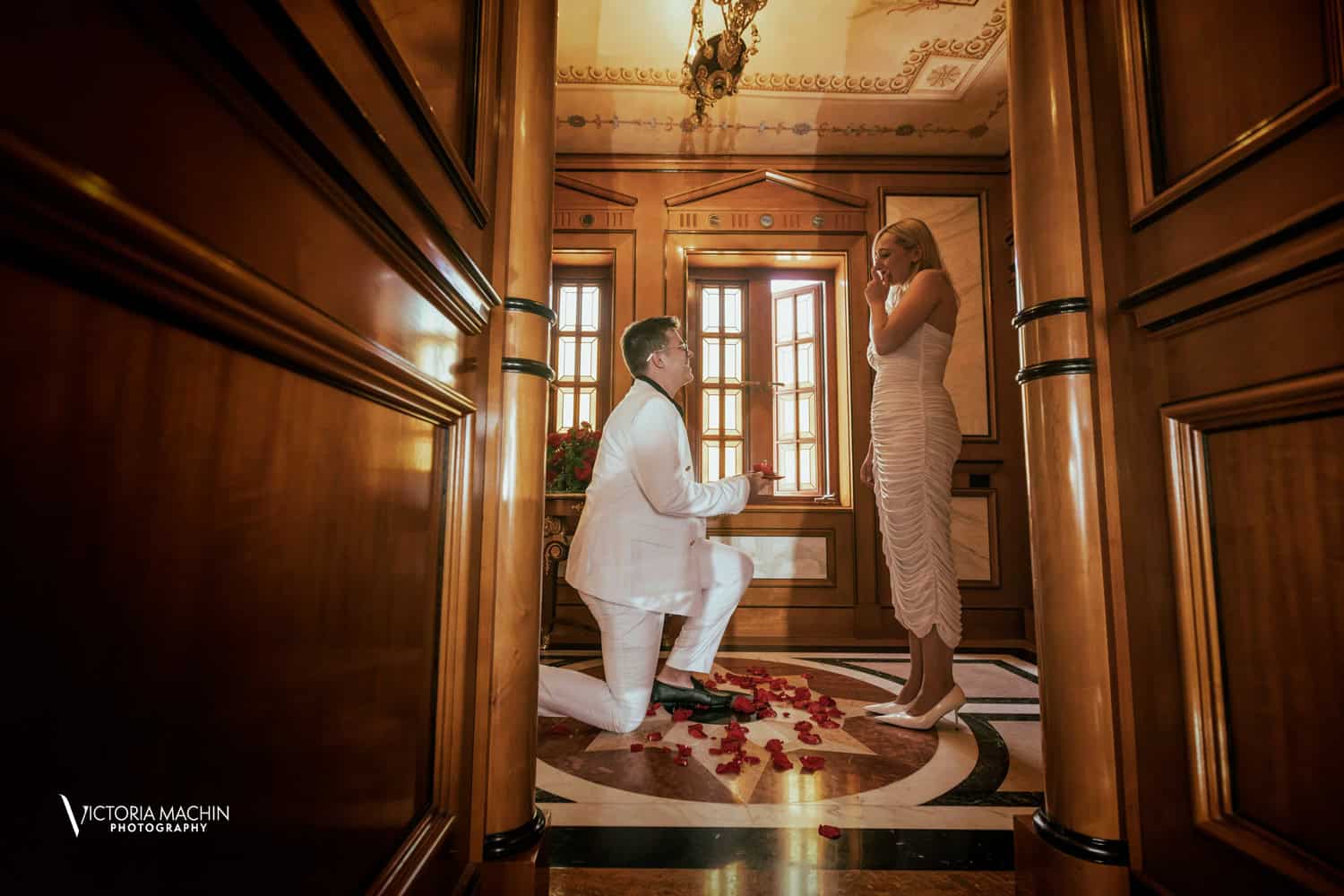 Surprise proposal on one knee among rose petals in a wood-paneled hall at Villa Casa Casuarina (Versace Mansion)