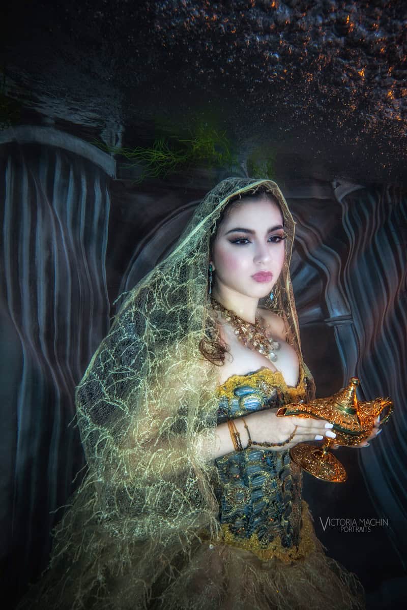 Young woman in a gold lace veil and corset holding a genie lamp in an Arabian Nights underwater set