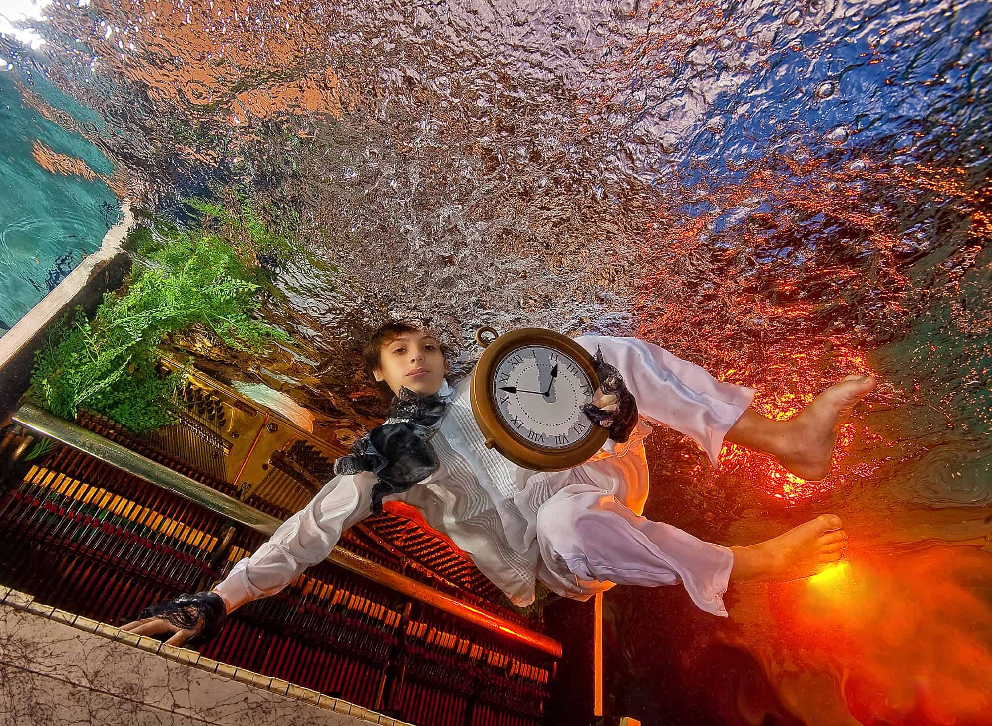 Boy in a white ruffled shirt holding a giant pocket watch beside a piano in a Wonderland underwater scene