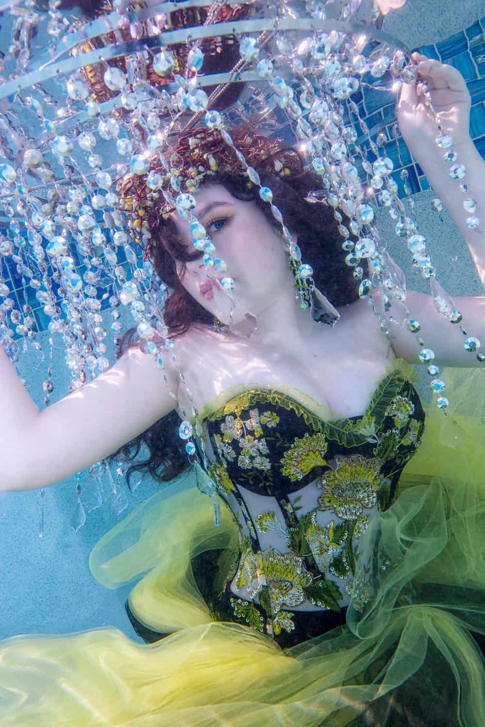 Young woman in an embroidered green corset beneath a crystal chandelier underwater