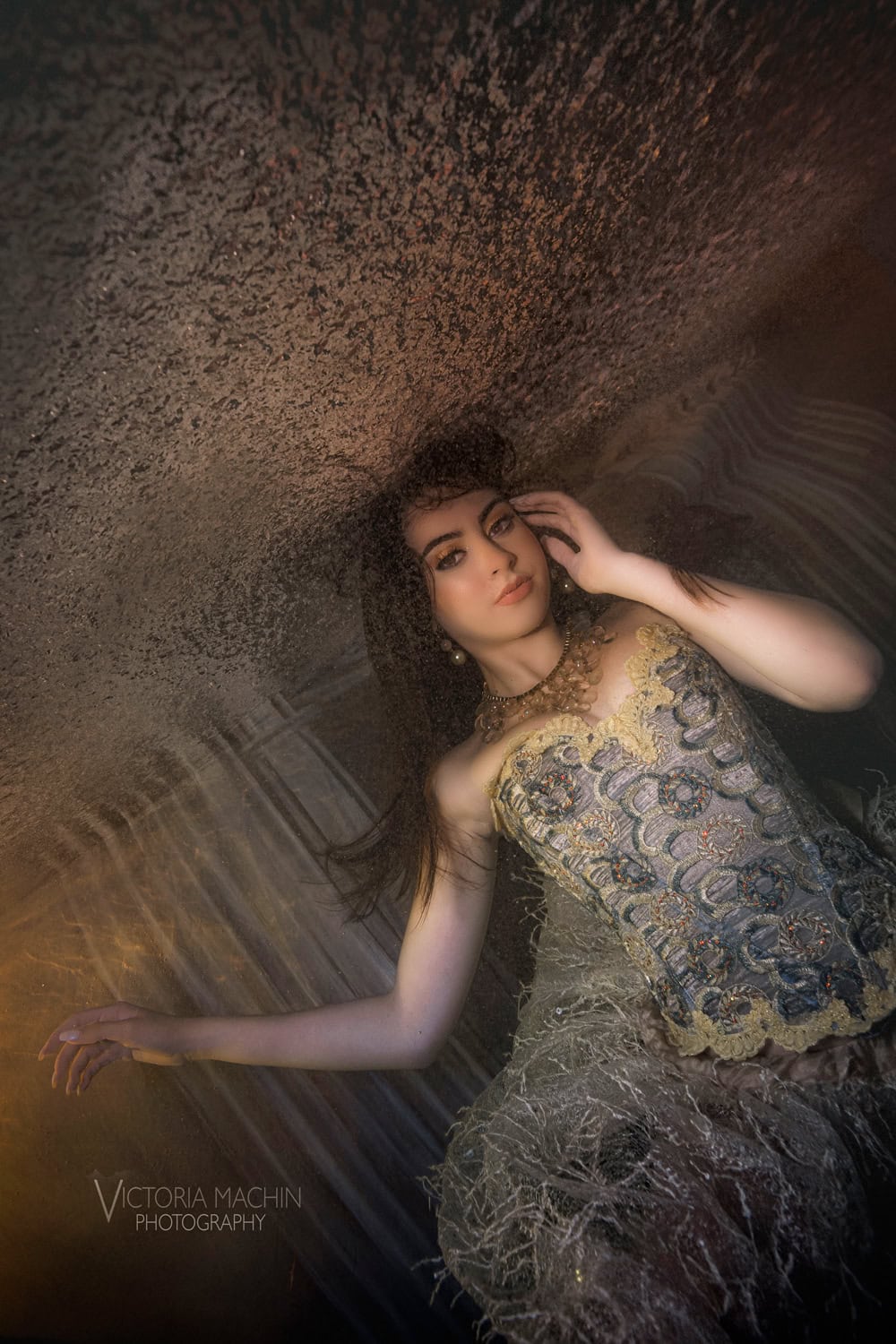 Young woman in a gold embroidered corset and pearl earrings floating in amber light