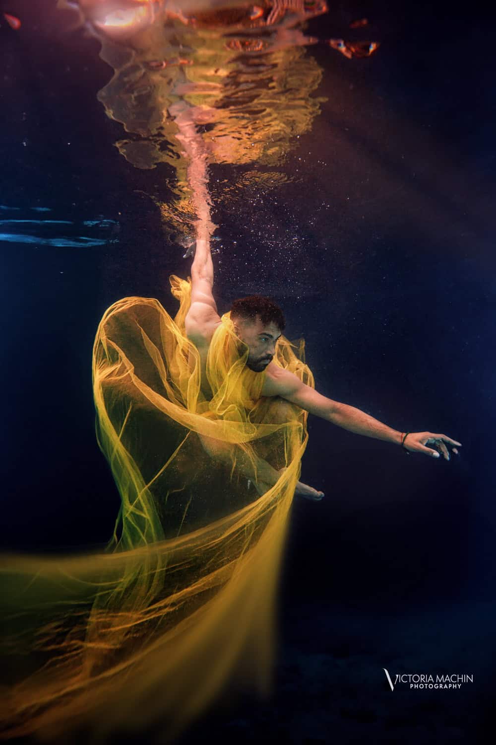 Man wrapped in golden yellow tulle reaching upward through dark water