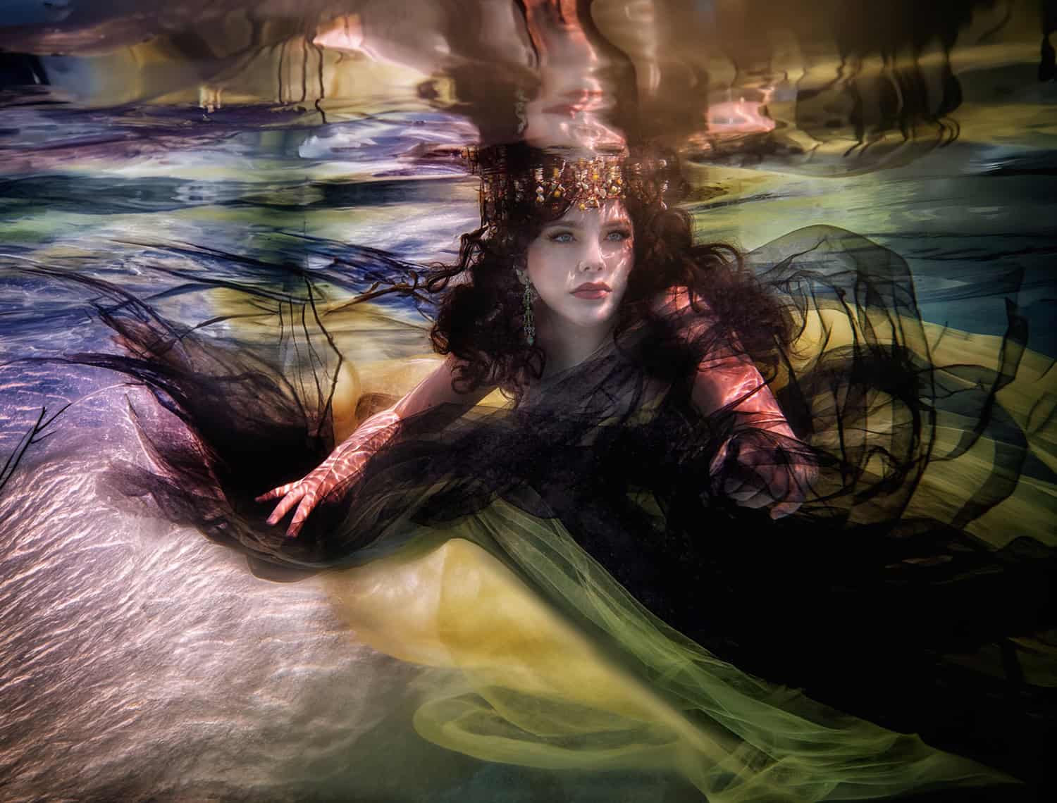 Quinceañera in a jeweled crown and black tulle gazing through golden underwater light