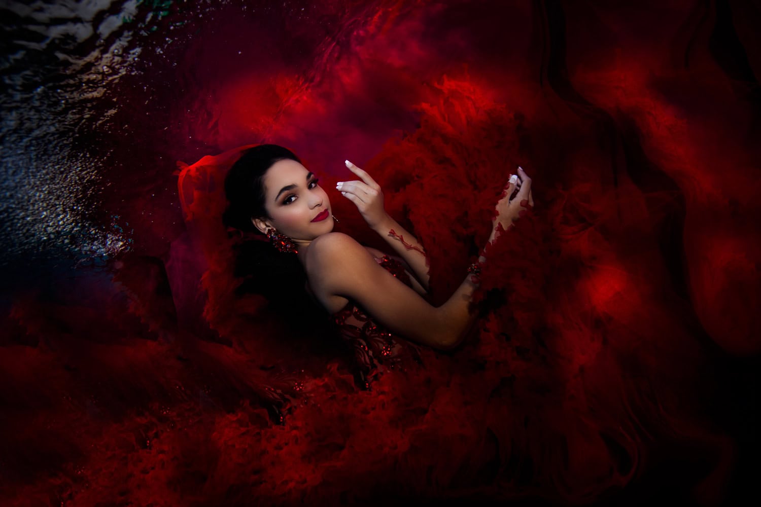 Quinceañera in a red gown looking back over her shoulder in a cloud of red tulle