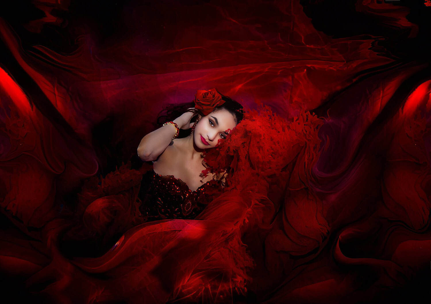 Quinceañera in a sequined red gown surrounded by swirling red fabric underwater