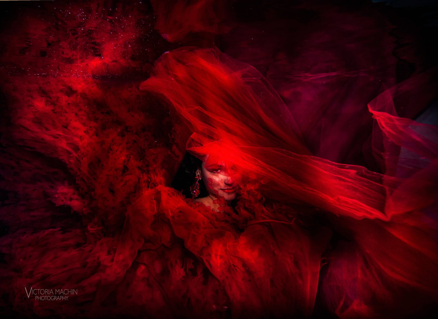 Quinceañera’s face glimpsed through layers of red tulle underwater