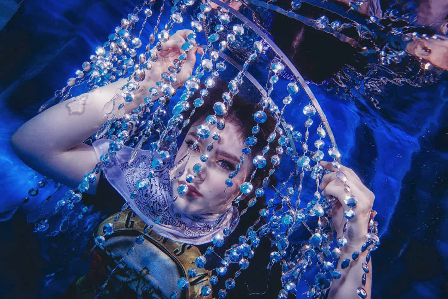Teen gazing through strands of crystals in deep blue water