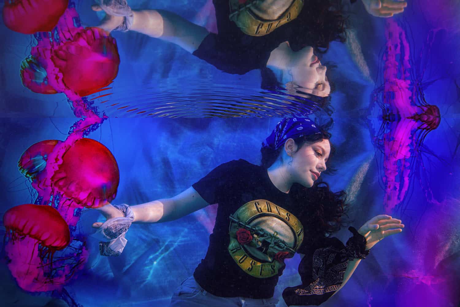 Teen in a band t-shirt and bandana floating among red jellyfish in electric blue water
