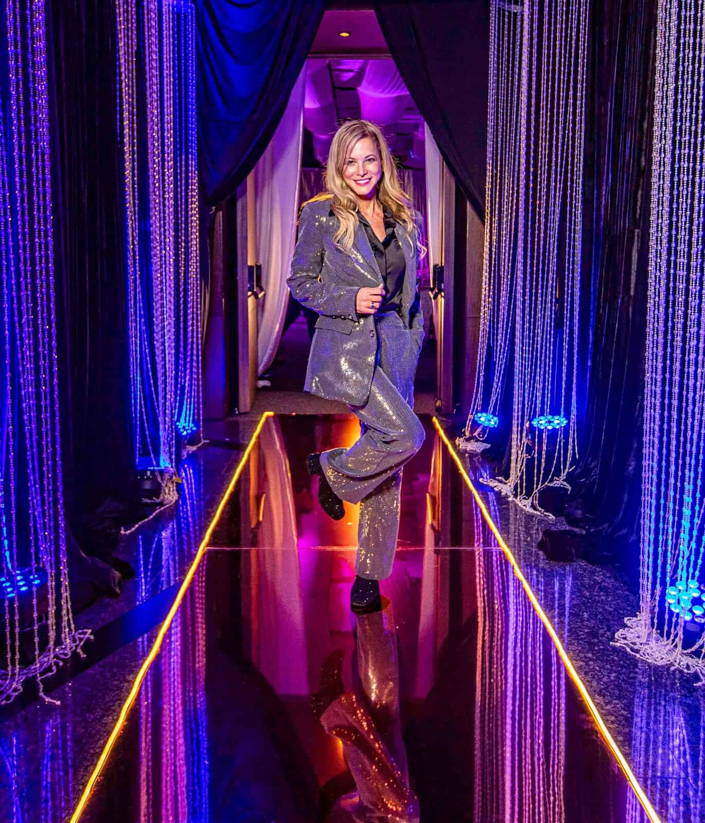 Victoria Machin in a sequin suit on a mirrored runway between crystal-beaded columns at an event