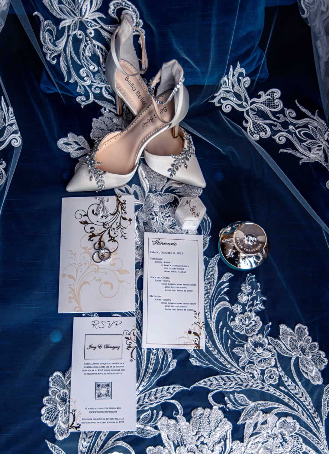 Wedding details flat lay on navy silk and lace: Bella Belle heels, invitation suite, rings and perfume